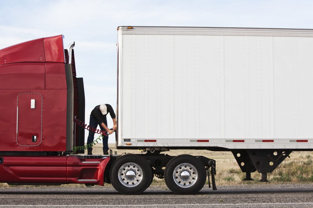 View of a driver connectiing the power cables to trailer of a commercial truck.